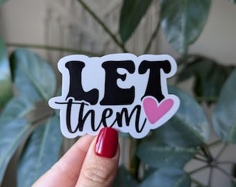 May include: A white sticker with the words "LET them" in black, outlined in black. The word "them" is in a cursive font. A pink heart is next to the word "them".