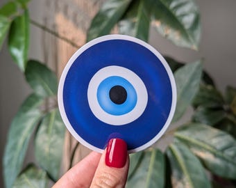 May include: A blue and white evil eye sticker with a white circle around the eye. The eye is blue with a black pupil.