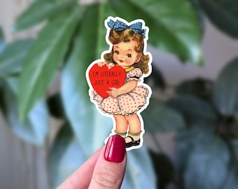 Può includere: Un adesivo in stile vintage con una bambina dei cartoni animati che tiene in mano un cuore rosso. Il cuore recita "I'M LITERALLY JUST A GIRL". La bambina indossa un vestito a pois, un fiocco blu e ha i capelli castani ricci. L'adesivo ha un bordo bianco.
