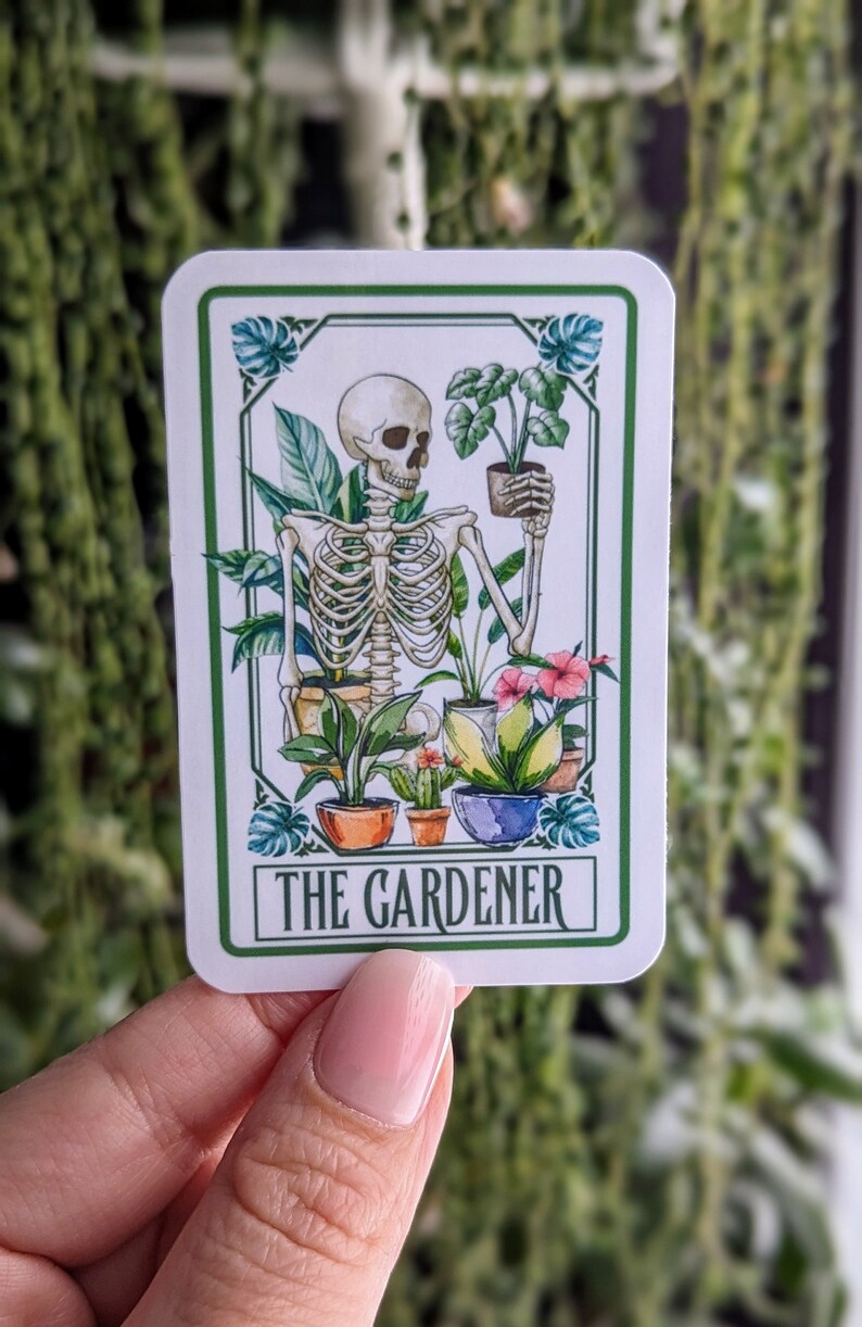 Puede incluir: Una pegatina blanca con borde verde muestra un esqueleto sosteniendo una planta en maceta. El esqueleto est&aacute; rodeado de otras plantas en maceta y flores. El texto "THE GARDENER" est&aacute; impreso en verde en la parte inferior de la pegatina.