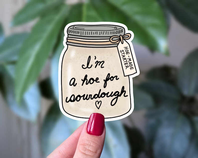 May include: A die-cut sticker shaped like a glass mason jar filled with beige sourdough starter. The jar features the black text 'I'm a hoe for sourdough' with a small heart and a tag reading 'HOE-MADE STARTER' tied with a string around the lid.