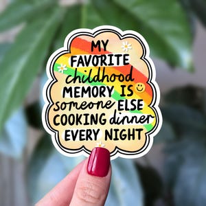 May include: A sticker with the text "MY FAVORITE childhood MEMORY IS someone ELSE COOKING dinner EVERY NIGHT." The sticker has a white border and a rainbow-coloured cloud design. Small white flowers are on the sticker.