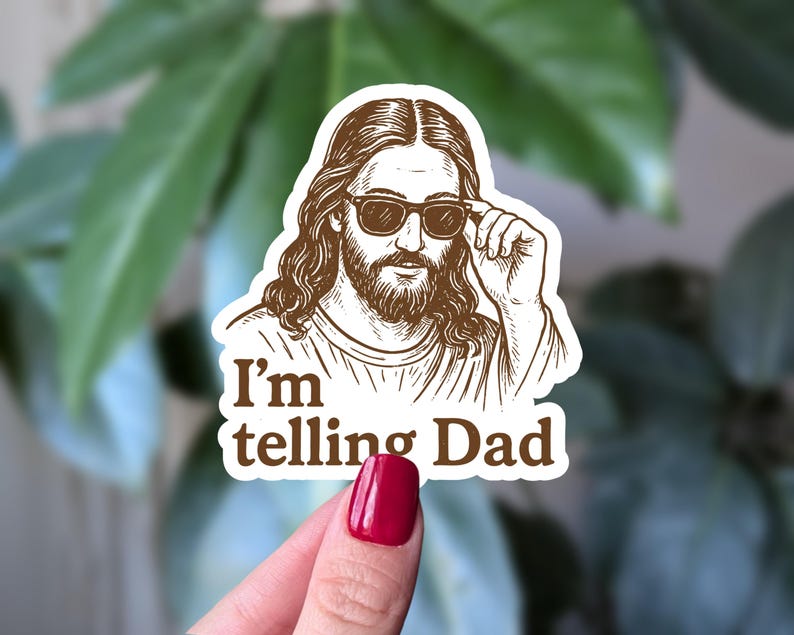 May include: A brown sticker featuring a stylized illustration of a figure wearing sunglasses, with long hair and a beard. The text "I'm telling Dad" is below the image. The sticker is held by a hand with red nail polish.
