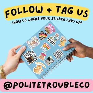 May include: A light blue spiral-bound notebook covered in various colorful stickers featuring cartoon animals, food, and text. The text on the notebook cover reads FOLLOW + TAG US SHOW US WHERE YOUR STICKER ENDS UP! and @POLITETROUBLECO.