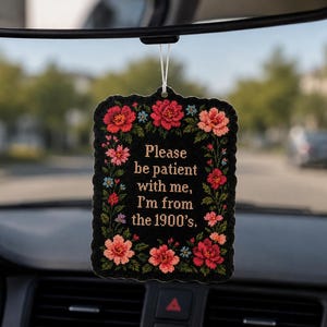 May include: Black air freshener with a floral design and the text "Please be patient with me, I'm from the 1900's." The air freshener is rectangular with a scalloped edge and is decorated with red, pink, and blue flowers.