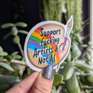 Może przedstawiać: Biała naklejka z tęczą i paletą farb. Naklejka głosi "Support fucking Artists & Not AI!"