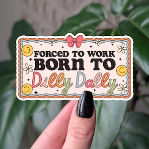 May include: A rectangular sticker with the text "FORCED TO WORK BORN TO DILLY DALLY" in a retro font. The sticker has a peach background with a light orange border, a pink bow, and smiley faces.
