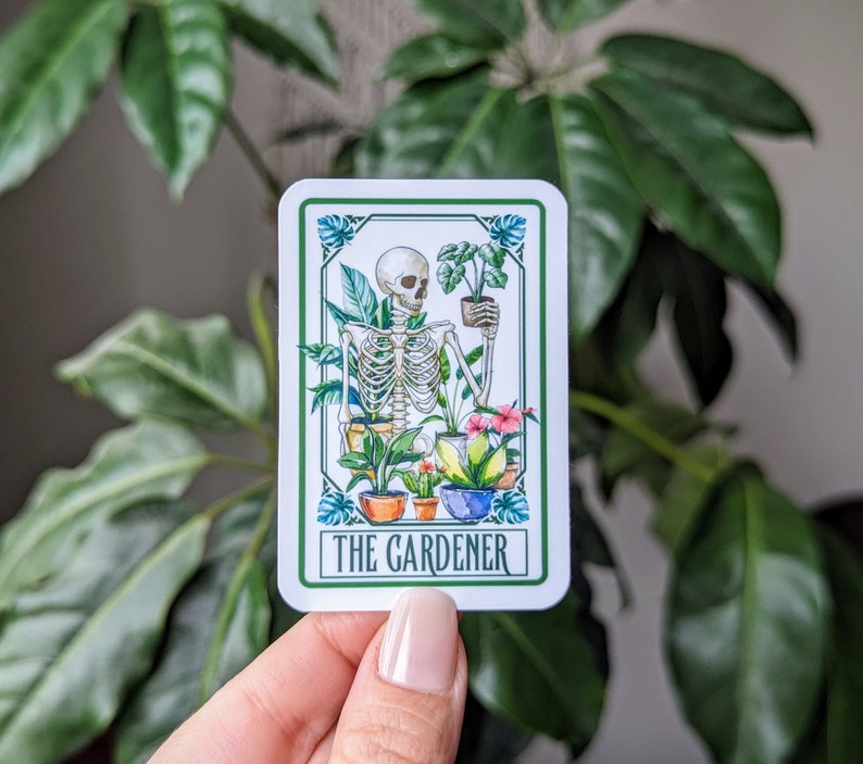Puede incluir: Una tarjeta blanca con un esqueleto sosteniendo una planta en maceta. La tarjeta tiene un borde verde y el texto "The Gardener" en letras negras.