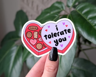 May include: A heart-shaped sticker with a purple background and the text "i tolerate you" in black. The sticker is open to reveal a box of chocolates with a red background and pink hearts.