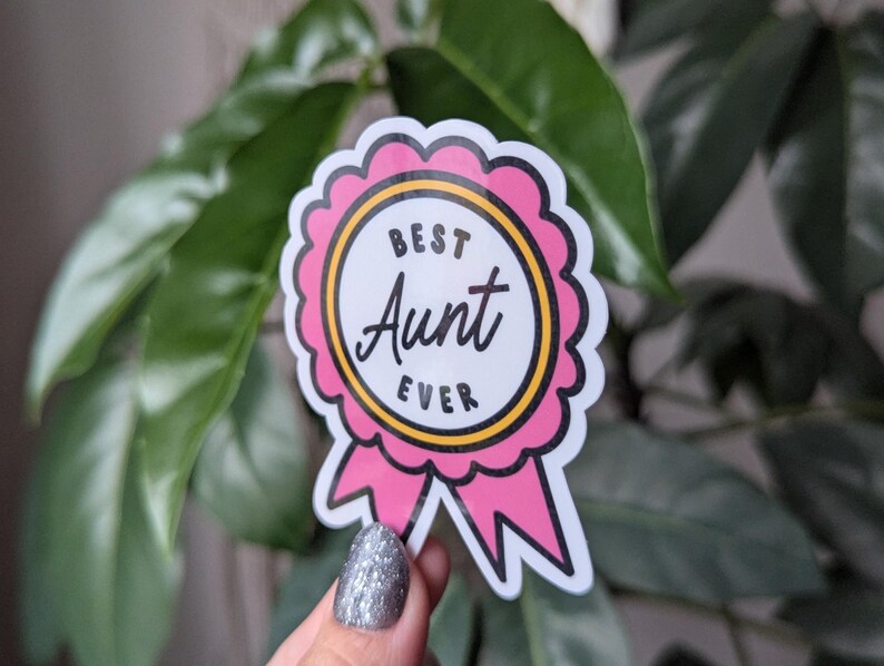 May include: A pink and yellow sticker with a white circle and the text "Best Aunt Ever" inside. The sticker is shaped like a ribbon.