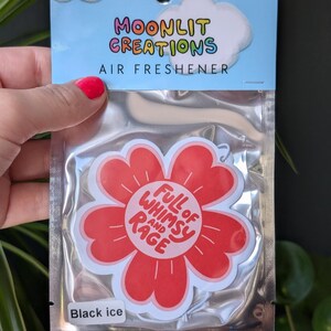 Może przedstawiać: Odświeżacz powietrza w przezroczystym plastikowym opakowaniu. Na g&oacute;rze opakowania znajduje się napis "Moonlit Creations Air Freshener" z grafiką chmury. Odświeżacz powietrza to czerwony kwiat z napisem "Full of Whimsy and Rage".