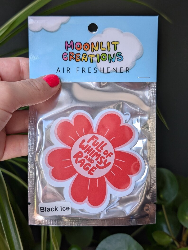 Może przedstawiać: Odświeżacz powietrza w przezroczystym plastikowym opakowaniu. Na g&oacute;rze opakowania znajduje się napis "Moonlit Creations Air Freshener" z grafiką chmury. Odświeżacz powietrza to czerwony kwiat z napisem "Full of Whimsy and Rage".