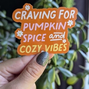 May include: Orange sticker with white text that reads "Craving for Pumpkin Spice and Cozy Vibes". The sticker has small white flower accents.