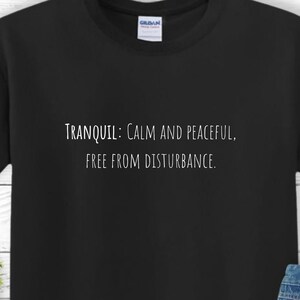 May include: Black t-shirt with white text that reads "TRANQUIL: CALM AND PEACEFUL, FREE FROM DISTURBANCE."