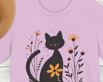 May include: Lilac t-shirt with a black cat sitting in a field of yellow flowers. The cat has a yellow flower on its back.
