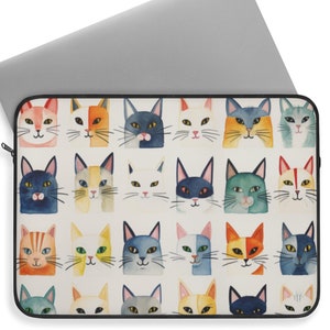 Pode incluir: Uma capa para laptop com fundo branco e um padrão repetido de rostos de gatos coloridos. Os gatos têm pelagem e olhos de diferentes cores, e alguns têm listras ou manchas.
