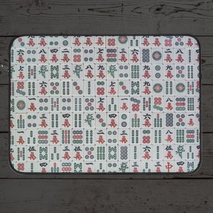May include: A white laptop sleeve featuring a repeating pattern of mahjong tiles. The tiles are white with black, red, and green markings. The sleeve has a black zipper.