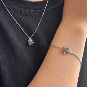 Puede incluir: Un conjunto de collar y pulsera de plata. El collar presenta un colgante con un diseño de trébol de cuatro hojas. La pulsera también tiene un dije de trébol. Ambas piezas son de plata.