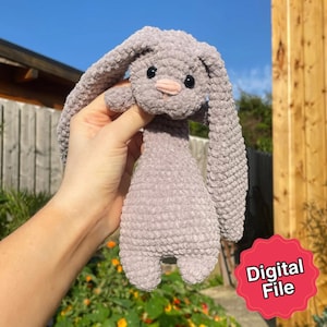 Könnte beinhalten: Ein handgefertigtes, graues Häschen aus Häkelarbeit mit langen Schlappohren und einer rosa Nase. Das Plüschtier hat schwarze Sicherheitsaugen. Das Bild enthält einen roten Aufkleber mit der Aufschrift "Digital File".