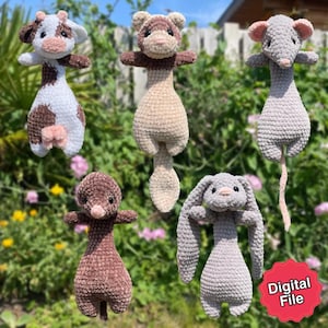 Könnte beinhalten: Eine Sammlung von fünf handgefertigten gehäkelten Stofftieren: eine Kuh, ein Frettchen, eine Maus, ein Maulwurf und ein Hase. Die Kuh ist weiß und braun, das Frettchen ist beige und braun, die Maus ist grau, der Maulwurf ist braun und der Hase ist grau. Die Tiere werden im Freien gezeigt.