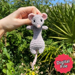 Könnte beinhalten: Eine handgefertigte graue Häkelmaus mit rosa Ohren, Nase und Schwanz. Die Maus hat kleine schwarze Augen und ausgestreckte Arme. Der Hintergrund ist ein üppiger grüner Garten. Ein roter Aufkleber mit den Worten "Digital File" befindet sich unten rechts.