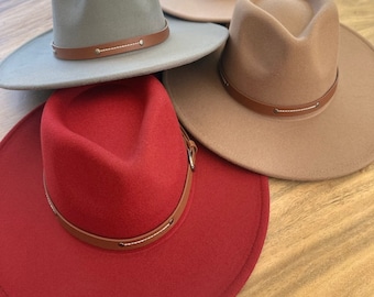 Cappello Fedora in feltro vegano: tesa larga, fascia con doppia fibbia, vestibilità regolabile.