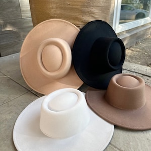 May include: Three felt hats in different colors: beige, black, and white. The hats have a wide brim and a flat crown.