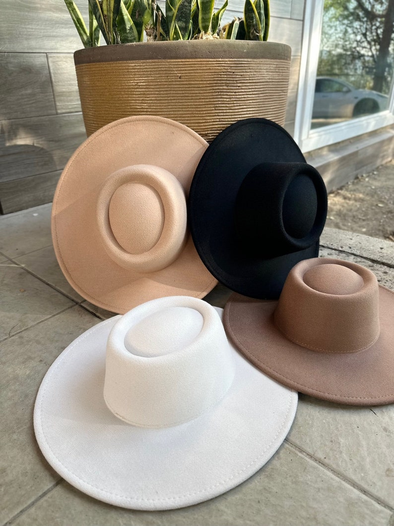 May include: Three felt hats in different colors: beige, black, and white. The hats have a wide brim and a flat crown.