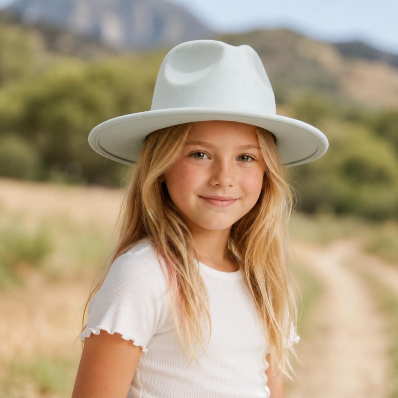 May include: A light blue fedora hat with a structured crown and a wide, flat brim. The hat features a smooth, felt-like texture and a matching tonal band around the base of the crown, providing a clean and uniform appearance for this headwear.
