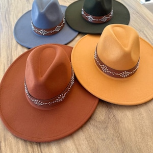 May include: Four felt fedora hats with a studded leather band. The hats are in shades of blue, green, orange, and brown.