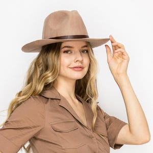 May include: A brown felt fedora hat with a brown leather band. The hat has a wide brim and a slightly indented crown.