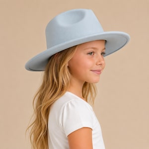 May include: A light blue fedora hat with a structured crown and a wide, flat brim. The hat features a smooth, felt-like texture and a matching light blue band around the base of the crown, providing a clean and uniform appearance for this headwear.