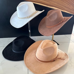 May include: Four cowboy hats in different colors: white, brown, black, and beige. Each hat has a brown leather band with a buckle.