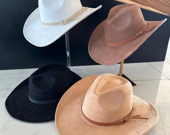 Peut inclure: Quatre chapeaux de cow-boy de couleurs différentes : blanc, marron, noir et beige. Chaque chapeau est doté d’une bande en cuir marron avec une boucle.