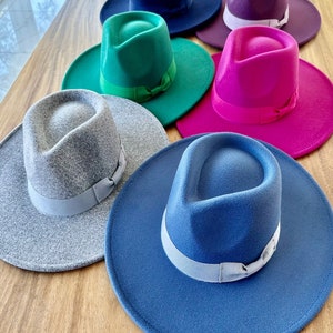 May include: Six felt fedora hats in various colors, including gray, green, blue, pink, purple, and navy blue. Each hat has a matching colored ribbon around the crown.
