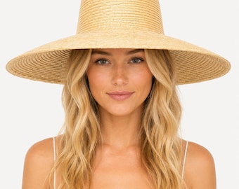 May include: A wide-brimmed straw hat in a natural tan color. The hat features a tall, cylindrical crown with a flat top and a wide, circular brim. The woven texture is consistent throughout the entire piece, creating a uniform appearance.