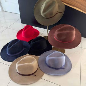 Puede incluir: Seis sombreros fedora de fieltro en varios colores, incluyendo rojo, azul, verde, marrón, beige y gris. Cada sombrero tiene una banda de color a juego alrededor de la corona.
