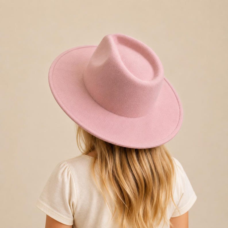 May include: A light pink fedora hat with a wide, flat brim and a structured, indented crown. The hat features a smooth, felt-like texture and a consistent pastel pink colour throughout, showcasing a clean, minimalist design with no additional trim.