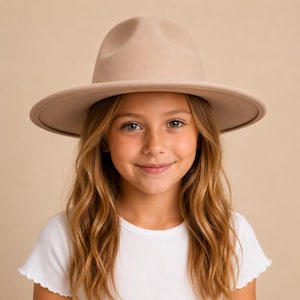 May include: A beige fedora hat with a structured crown and a wide, flat brim. The hat features a smooth, uniform texture and a matching tonal band around the base of the crown, providing a clean and simple appearance for this headwear accessory.