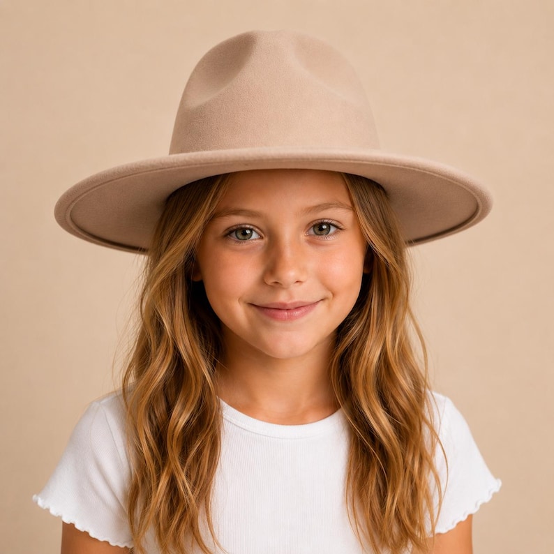 May include: A beige fedora hat with a structured crown and a wide, flat brim. The hat features a smooth, uniform texture and a matching tonal band around the base of the crown, providing a clean and simple appearance for this headwear accessory.