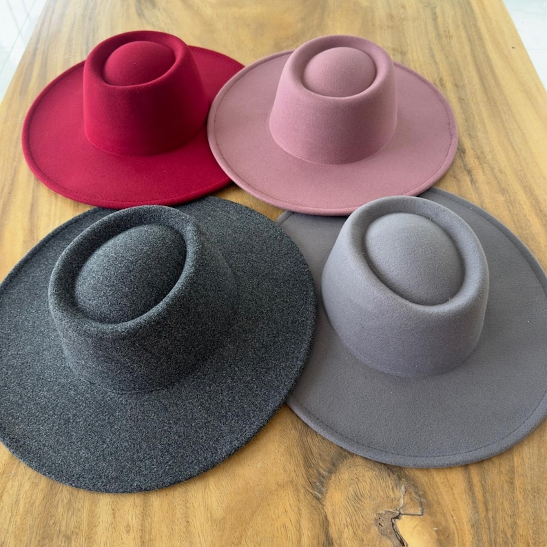May include: Four felt hats in different colors: red, pink, gray, and dark gray. The hats have a wide brim and a tall, round crown.