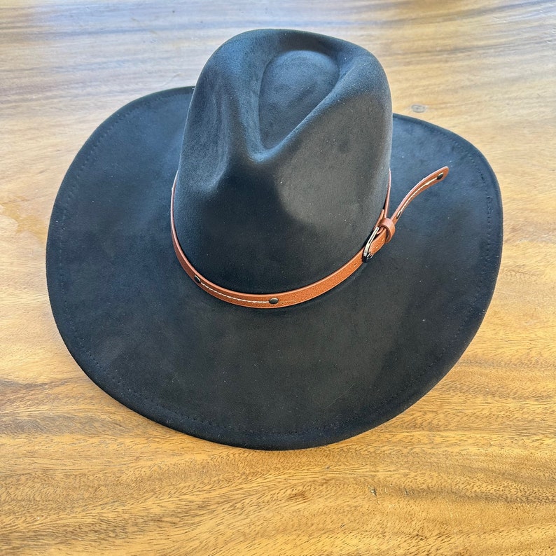 May include: A black fedora-style hat with a wide brim and a brown leather band. The hat has a suede-like texture and a classic, stylish design. The leather band is secured with small metal rivets.
