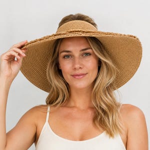 May include: A wide-brimmed straw visor hat in a natural tan color. The hat features a woven texture with a frayed, raw edge along the circumference of the brim. The design is open at the top, allowing for a comfortable fit while providing shade.