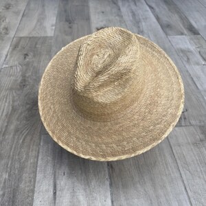 May include: A wide-brimmed straw hat with a woven texture. The hat is light brown in color and has a slightly rounded crown.