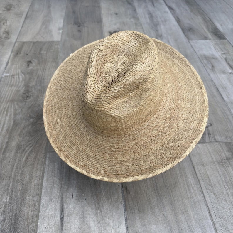 May include: A wide-brimmed straw hat with a woven texture. The hat is light brown in color and has a slightly rounded crown.