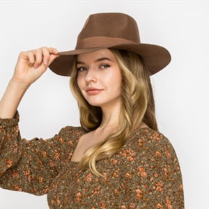 May include: A brown felt fedora hat with a wide brim. The hat is being worn by a person with long, wavy, light brown hair.
