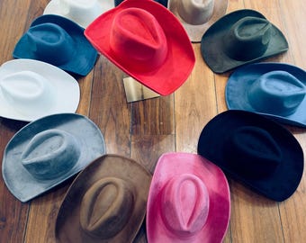 Peut inclure: Une collection de 11 chapeaux de cow-boy de différentes couleurs, dont le rouge, le rose, le marron, le noir, le gris et le bleu. Les chapeaux sont disposés en cercle sur une surface en bois.