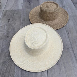 May include: Two straw hats, one in a light beige color and the other in a darker brown color. Both hats have a wide brim and a tall crown.