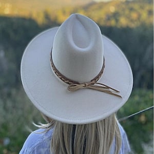 May include: A white felt fedora hat with a brown braided leather band and a long tassel. The hat has a wide brim and a slightly indented crown.