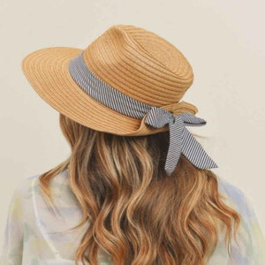 以下が含まれることがあります： 幅広のつばとストライプのリボンが後ろでリボン結びになっている麦わら帽子です。